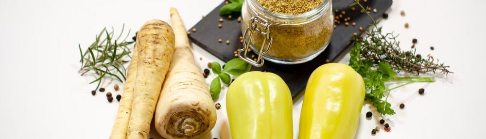 A flat lay of parsnips, bell peppers, herbs, and a spice jar on a white background.