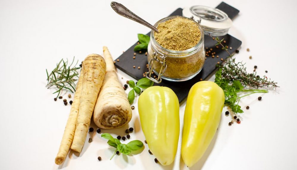 A flat lay of parsnips, bell peppers, herbs, and a spice jar on a white background.
